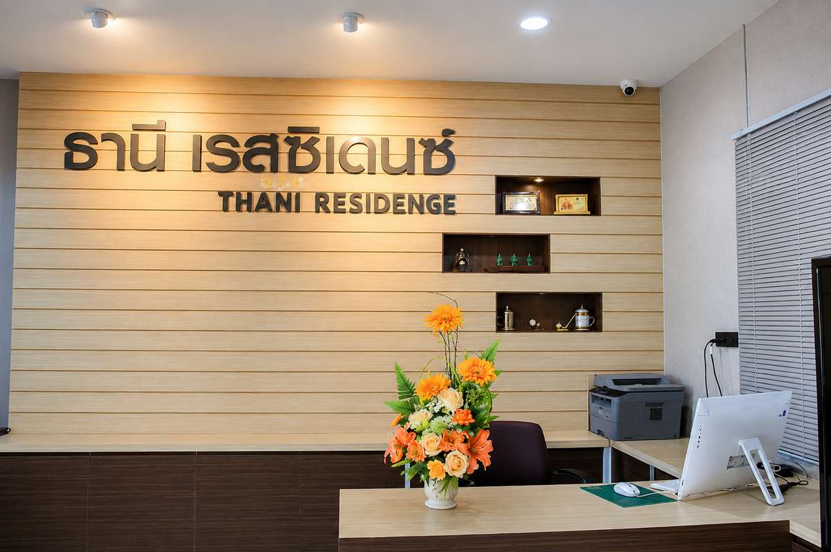 Reception desk at Thani Residence with the wooden logo wall and fresh orange flowers